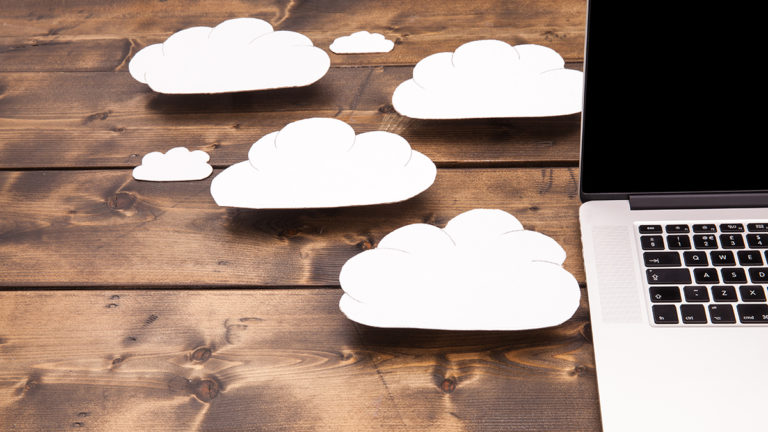 White paper clouds next to an open laptop on a wooden desk